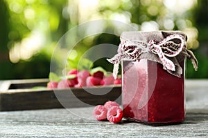 Glass jar with tasty raspberry jam on table against blurred background