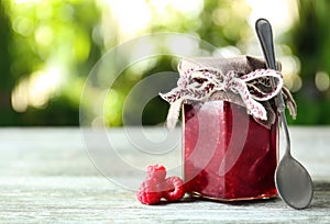 Glass jar with tasty raspberry jam on table against blurred background