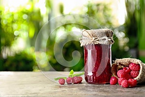 Glass jar with tasty raspberry jam on table against blurred background