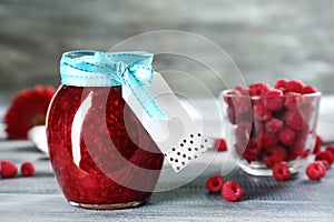 Glass jar with tasty raspberry jam on wooden table