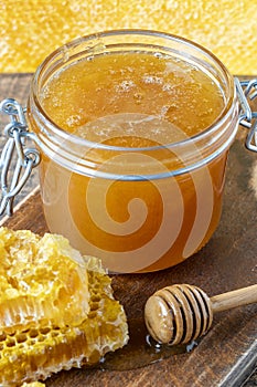 A glass jar of thick golden honey with wooden spoon and honeycombs. Concept of beekeeping, apiculture, apiary. Sweet honey product