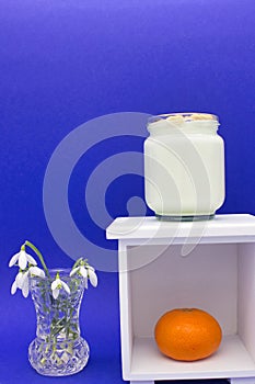 A glass jar of yogurt and an orange on a white shelf