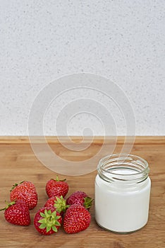 Glass jar with yogurt and seven strawberries on a wooden background.