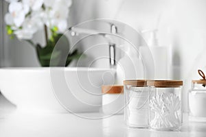 Glass jars with cotton pads and swabs on white countertop in bathroom. Space for text