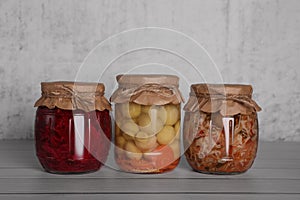 Glass jars with different preserved vegetables and mushrooms on wooden table