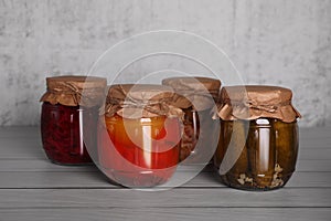 Glass jars with different preserved vegetables on wooden table