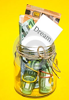 Glass jars filled with Euro bills, savings inside glass jar, money isolated on yellow background. Paper note written