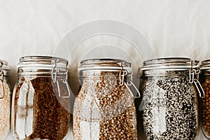 Glass jars full with dried uncooked food ingredients, red rice, barley pearls, sesame seeds, poppy seeds