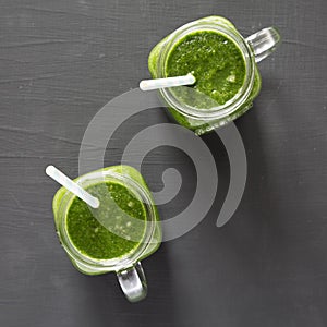 Glass jars full of green smoothie with spinach, avocado and banana over black background, top view. From above, overhead