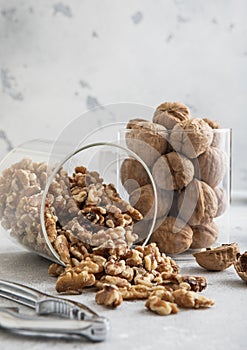 Glass jars with healthy raw walnut whole and peeled nuts on white kitchen table.Macro