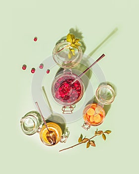 Glass jars with honey-fermented cranberries, lemon and carrot on a pink background