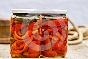Glass jars with pickled red bell peppers.Preserved food concept, canned vegetables isolated in a rustic composition