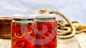 Glass jars with pickled red bell peppers.Preserved food concept, canned vegetables isolated in a rustic composition