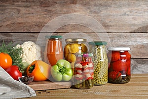 Glass jars with pickled vegetables on table against brown background
