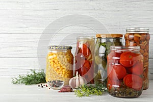 Glass jars with pickled vegetables on table against wooden background