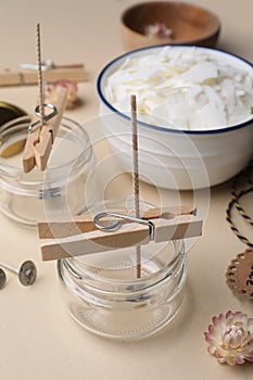 Glass jars with wicks and clothespins as stabilizers on beige background. Making homemade candles