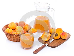 Glass and jug of apricot juice with a basket of apricots and sliced apricots on a cutting board