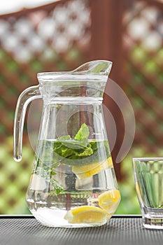 Glass jug of cold detox water with lemon slices and mint leaves. Refreshing drink in hot summer day.