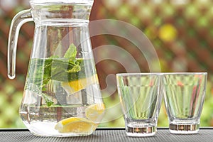 Glass jug of cold detox water with lemon slices and mint leaves. Refreshing drink in hot summer day.