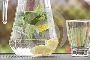 Glass jug of cold detox water with lemon slices and mint leaves. Refreshing drink in hot summer day.
