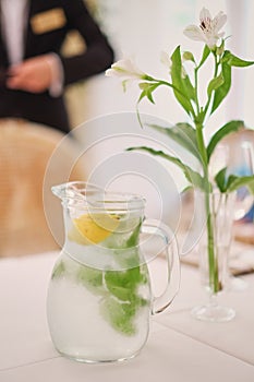 Glass jug of cold lemonade on a light background cafe. Pitcher lemon water with mint. Cold lemonade box