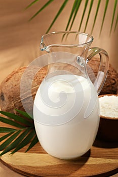 Glass jug of delicious vegan milk near coconuts on brown background
