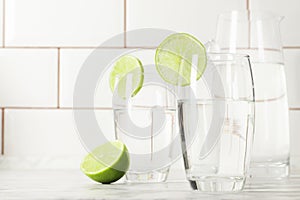 Glass and jug with fresh water and lime on marble table.