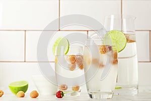 Glass and jug with fresh water and lime on marble table. Space for text. Flavored water. Summer drinks.