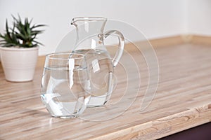 Glass and jug with fresh water on table in kitchen.