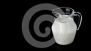 Glass jug of milk on black background with copy space