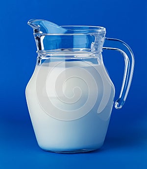 Glass jug of milk isolated on blue background