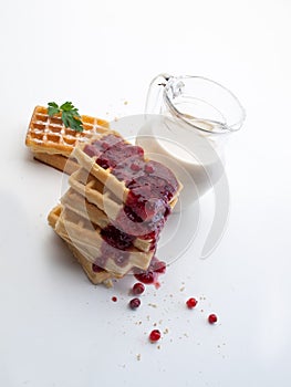 A glass jug with milk next to waffles and currant jam