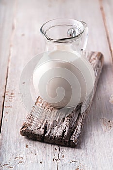 Glass jug with milk on the white wooden table