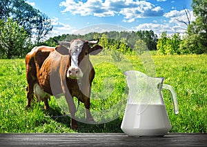 Glass jug with milk on wooden table with brown cow