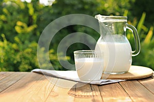 Glass and jug of tasty fresh milk on table outdoors, space for text