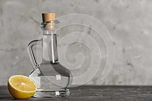 Glass jug with vinegar and lemon on table