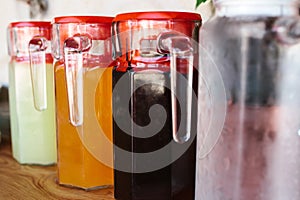 Glass jugs with variety of fruit and berry drinks with red lids stand on the table