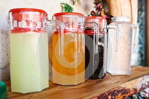 Glass jugs with variety of fruit and berry drinks with red lids stand on the table