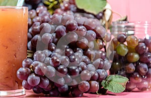 Glass of juice and bunches of grape on pink background