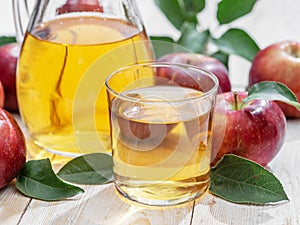 Glass of juice and carafe of fresh apple juice and organic apples on wooden table