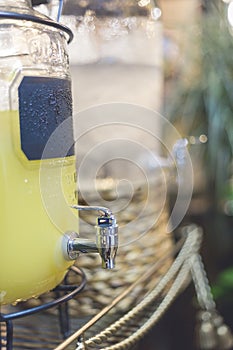 A glass juice dispenser containing lemonade with a stainless steel spigot, with another water dispenser beside it. At an outdoor