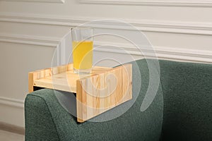 Glass of juice on sofa with wooden armrest table in room. Interior element