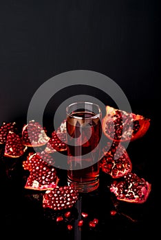 Glass of juice with a some pieces of pomegranate on a black background.