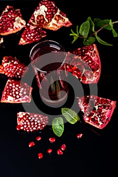 Glass of juice with a some pieces of pomegranate on a black background.