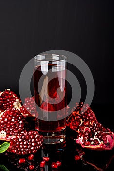 Glass of juice with a some pieces of pomegranate on a black background.