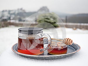 Sklenená kanvica horúceho čaju a pohár medu na stole pokrytom snehom