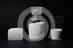 Glass laboratory jar with samples of white synthetic rubber and a cube of white rubber next to it on a black background