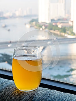 Glass of lager beer on edge of window with Bangkok skyscraper buildings cityscape view in background