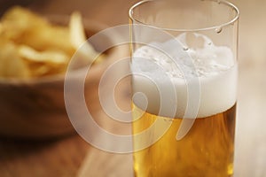 Glass of lager beer with potato chips on wooden table