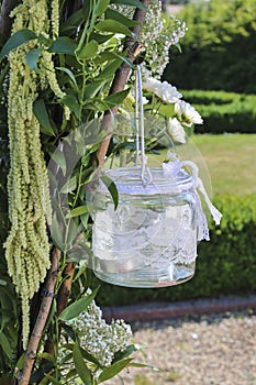 Glass lantern decorated with white lace hanging on wedding archw